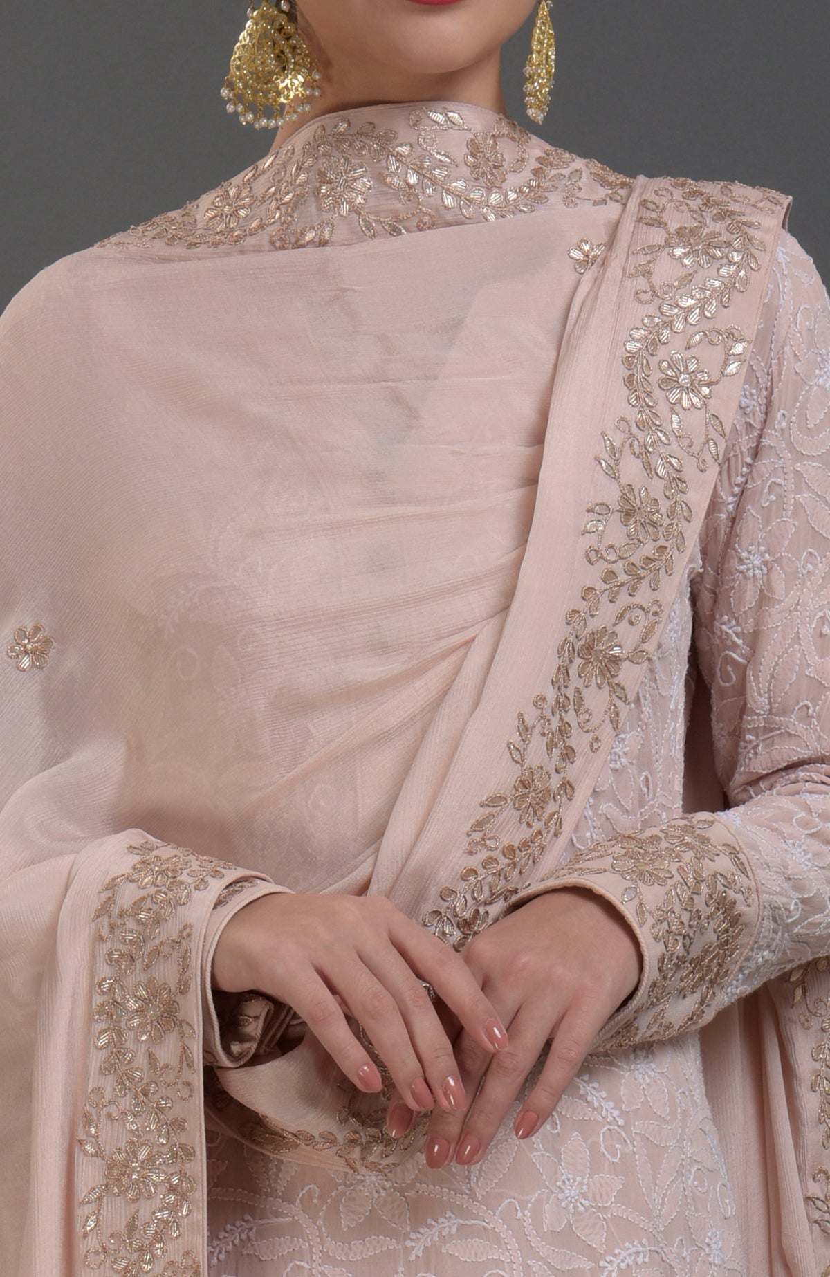 A woman models an oyster pink Chikankari and Gota Patti hand-embroidered sharara suit.