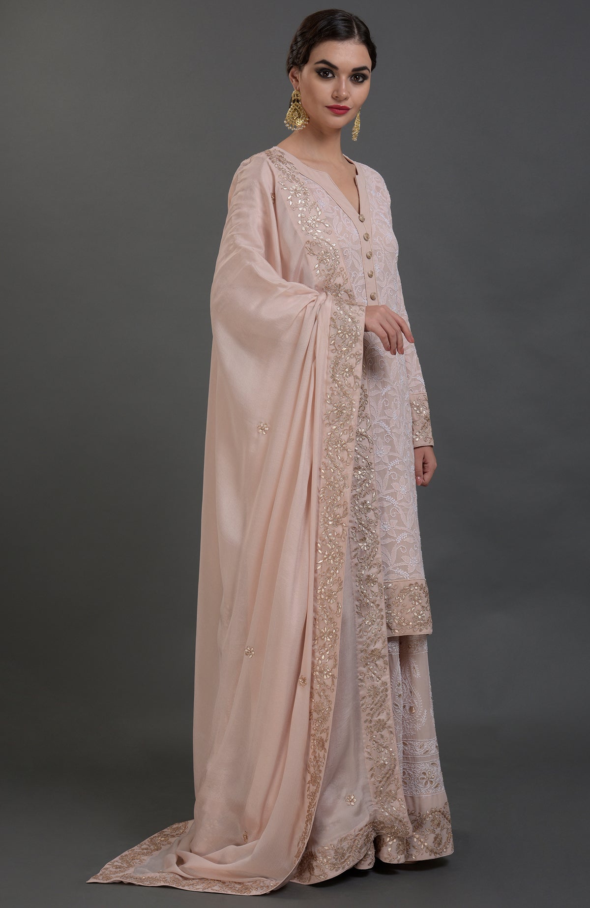 A woman models an oyster pink Chikankari and Gota Patti hand-embroidered sharara suit.