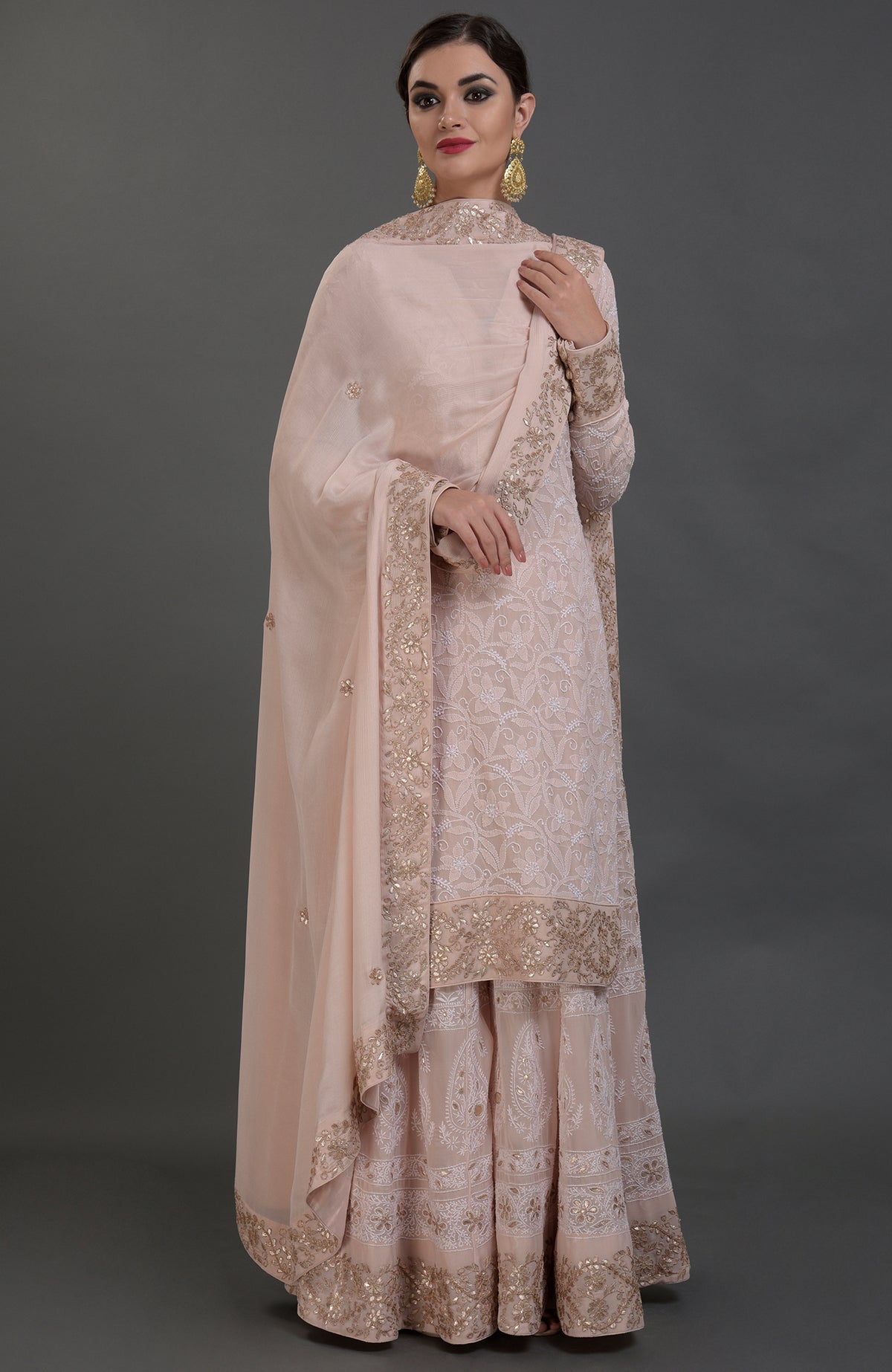 A woman models an oyster pink Chikankari and Gota Patti hand-embroidered sharara suit.