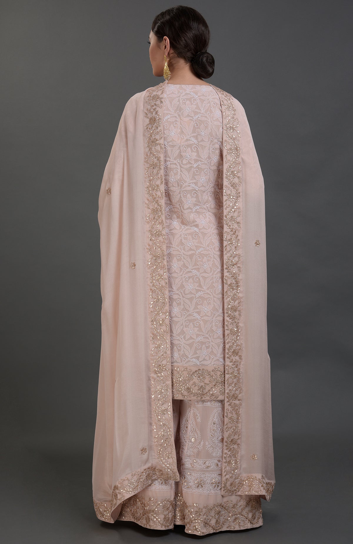 A woman models an oyster pink Chikankari and Gota Patti hand-embroidered sharara suit.