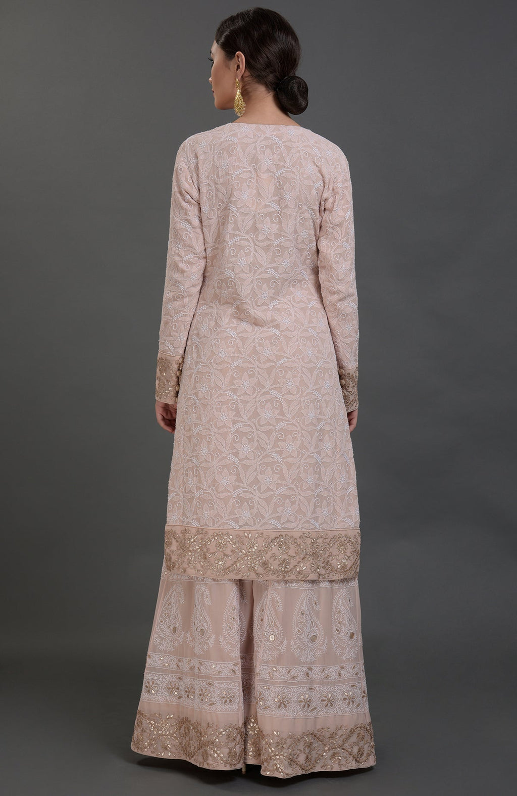 A woman models an oyster pink Chikankari and Gota Patti hand-embroidered sharara suit.