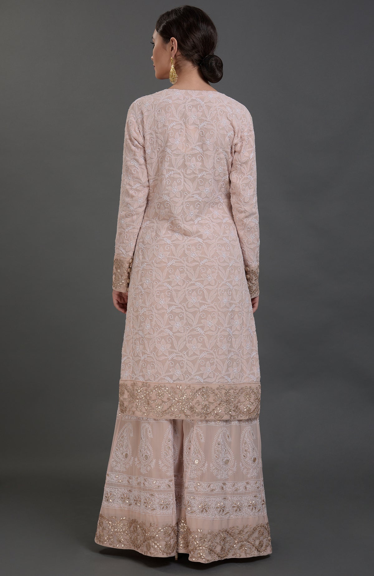 A woman models an oyster pink Chikankari and Gota Patti hand-embroidered sharara suit.