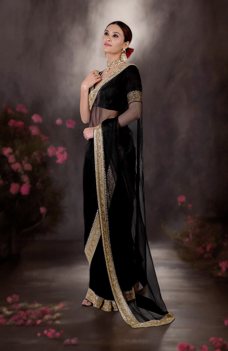 A woman models a black saree with gold and silver zardozi embroidery.