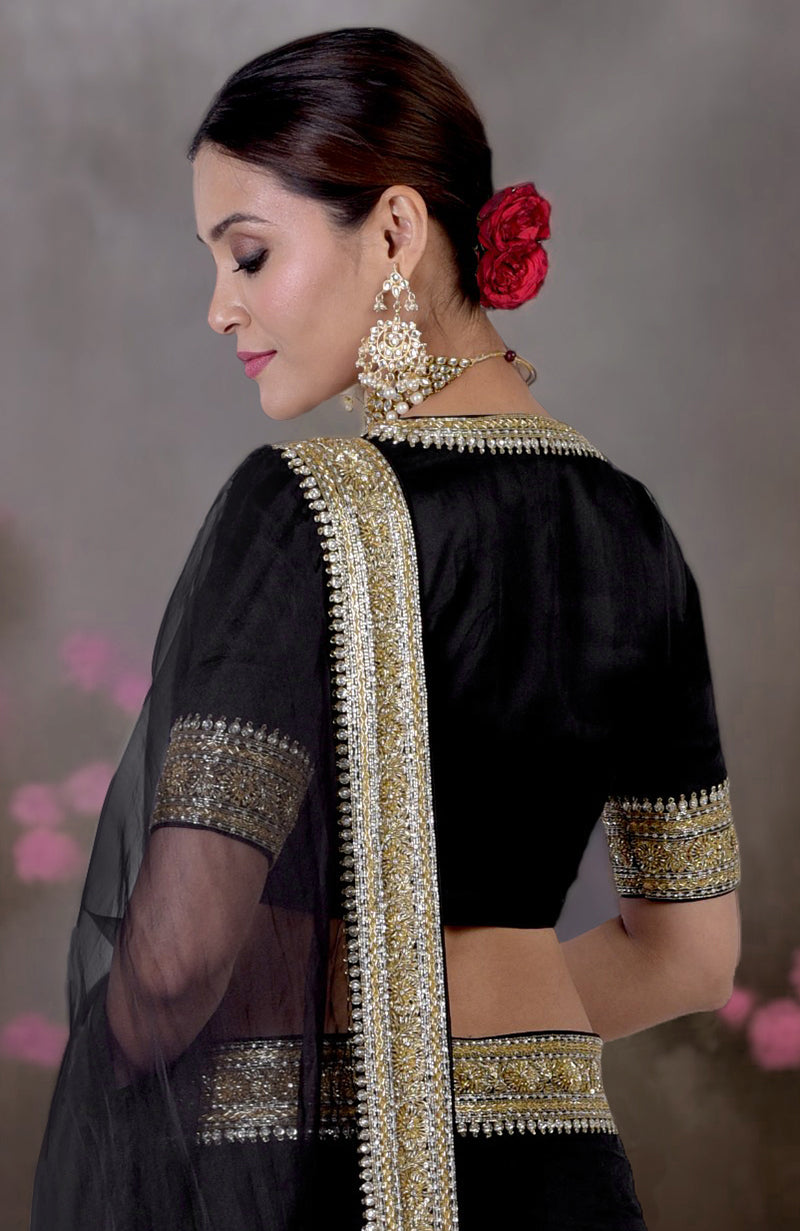 A woman in a black saree with gold and silver embroidery and large earrings.