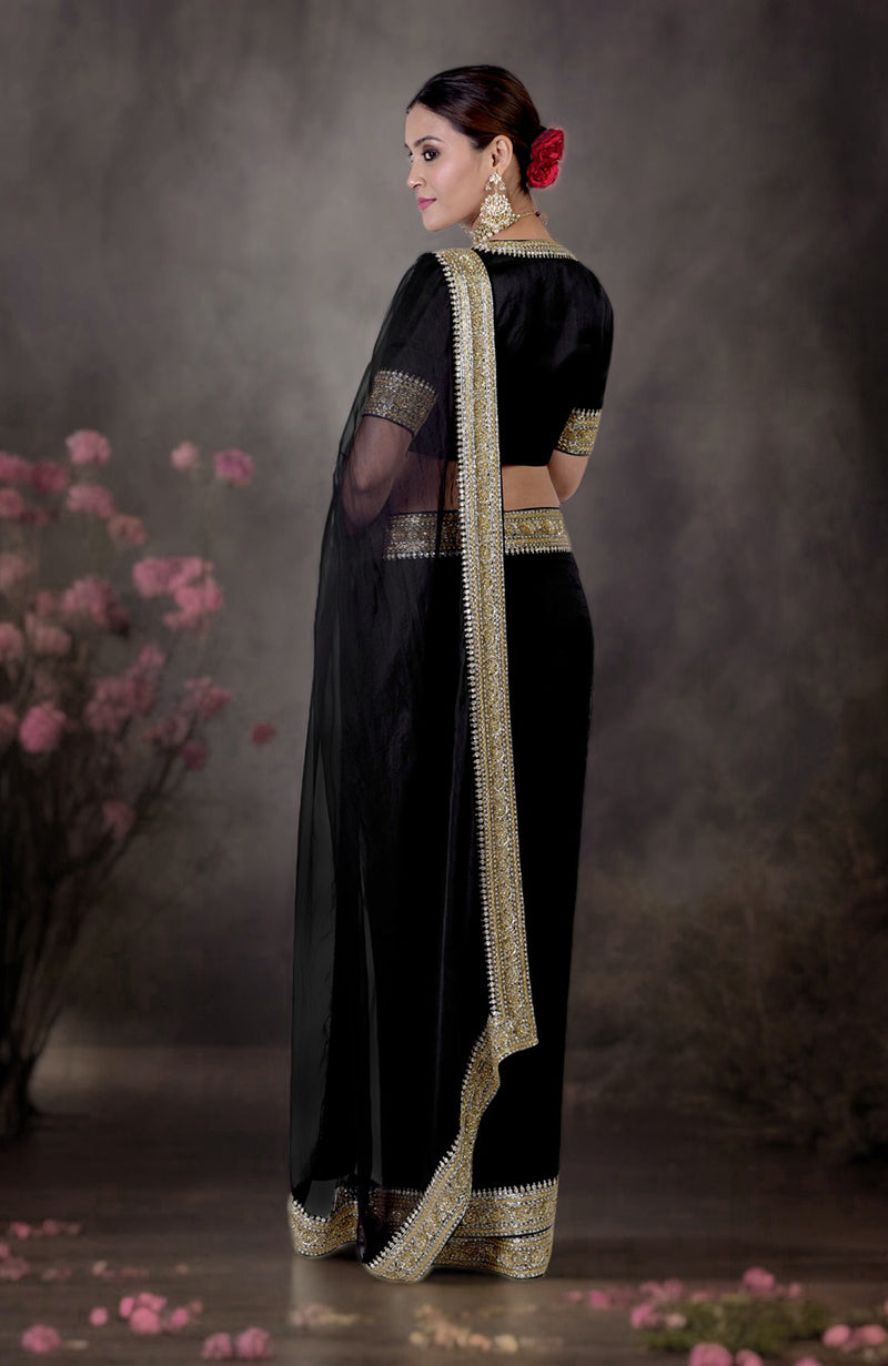 A woman models a black saree with gold and silver zardozi embroidery.