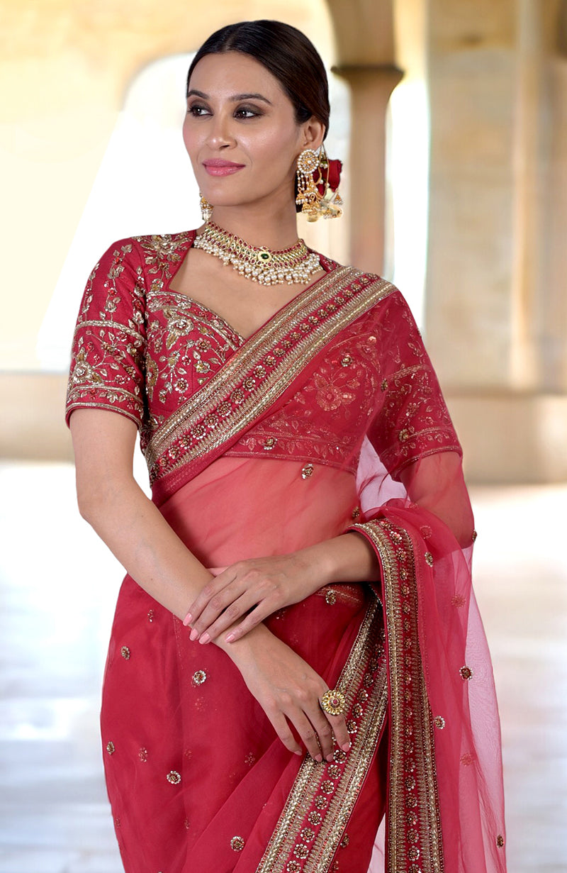 A woman in a ruby red zardozi hand-embroidered saree with a matching blouse.