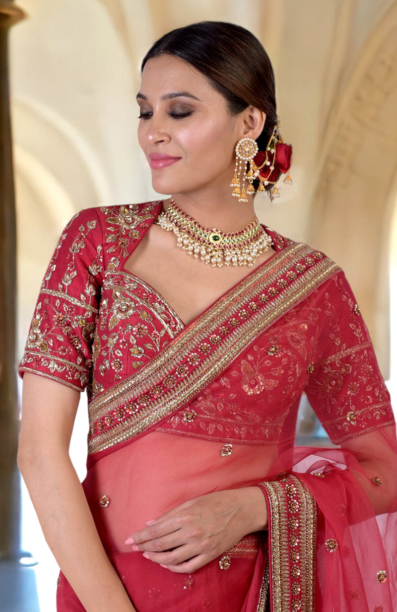 A woman in a ruby red zardozi hand-embroidered saree with a matching blouse.
