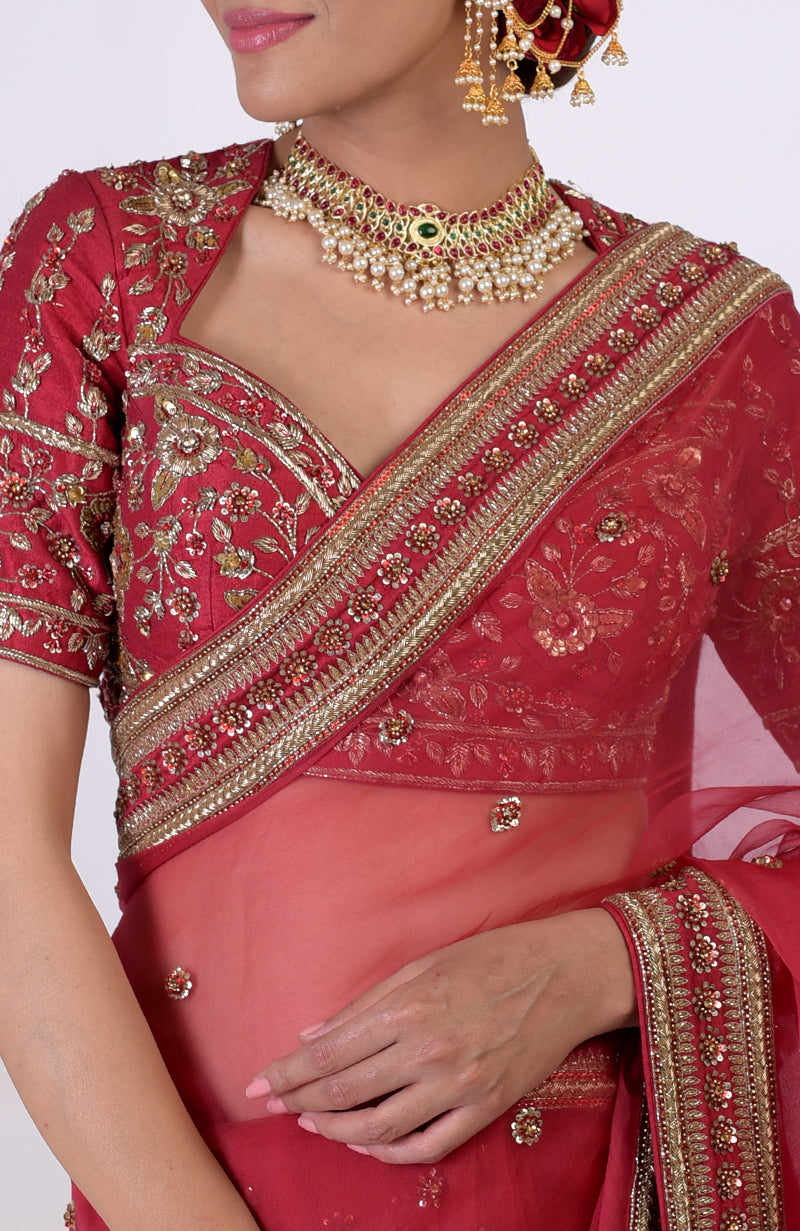 A woman in a ruby red zardozi hand-embroidered saree with a matching blouse and jewelry.