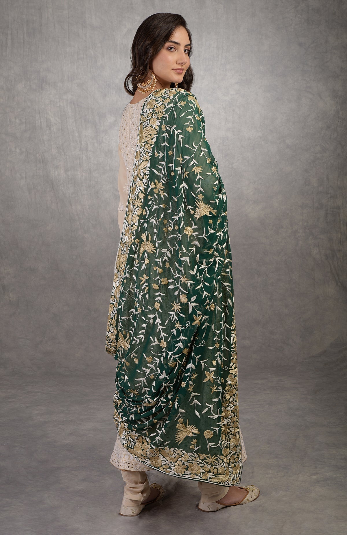 A woman in a champagne chikankari suit with a green Parsi Gara dupatta.