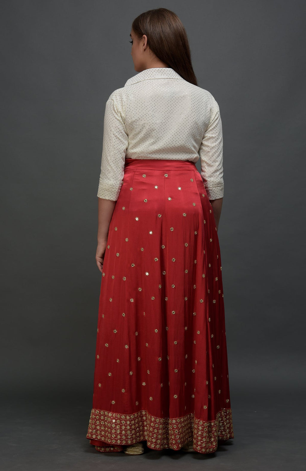 A woman from behind wears a white polka dot blouse and a red mirror work skirt.