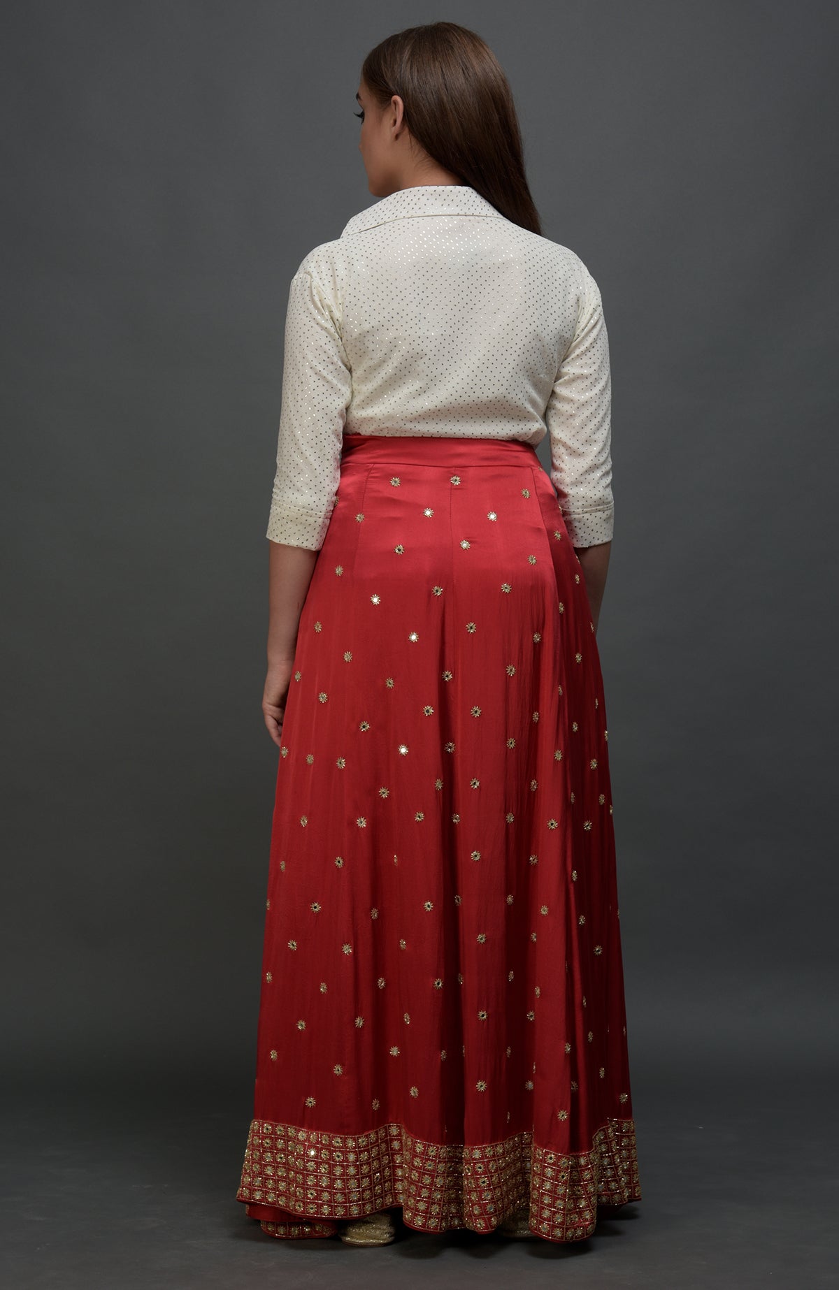 A woman from behind wears a white polka dot blouse and a red mirror work skirt.