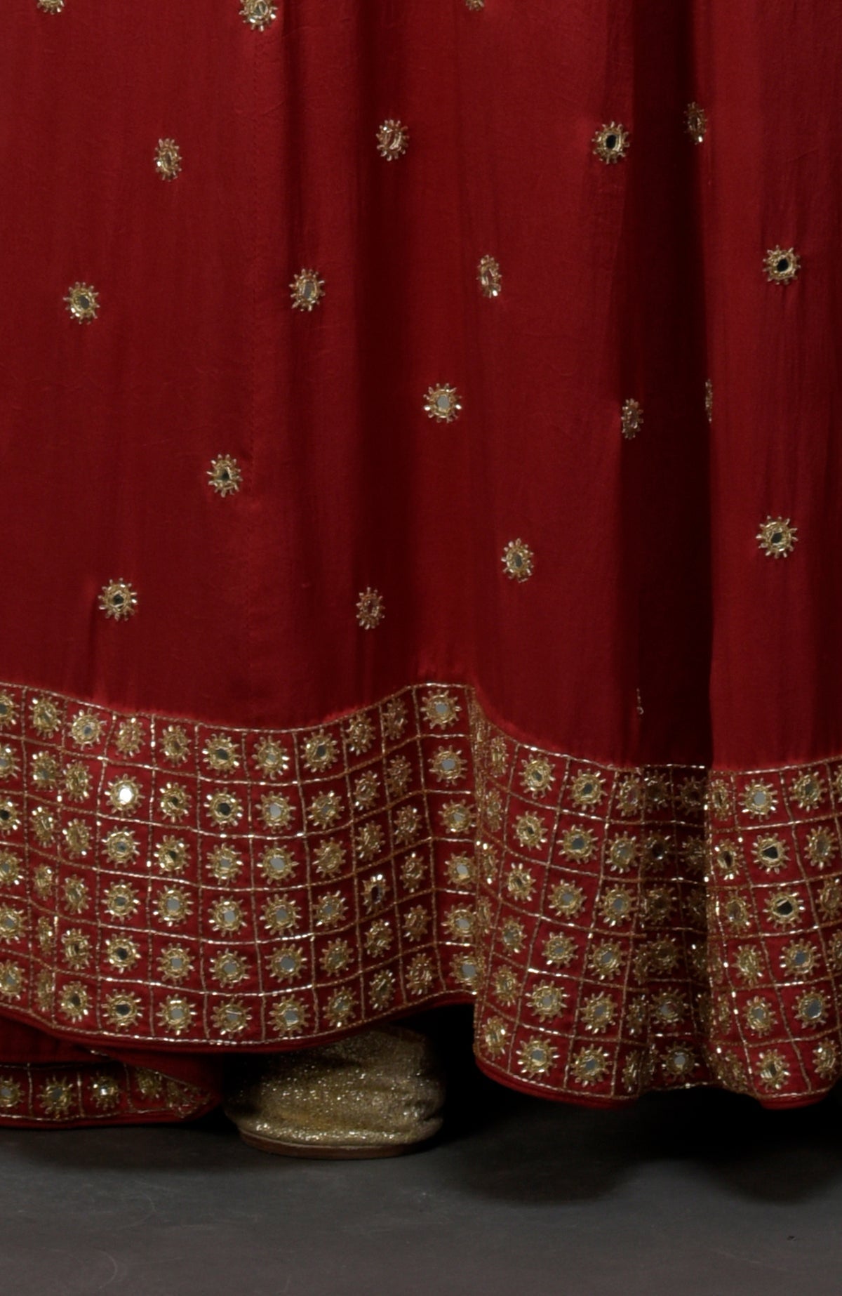 A royal red skirt with gold mirror and zardozi work, revealing a gold shoe.