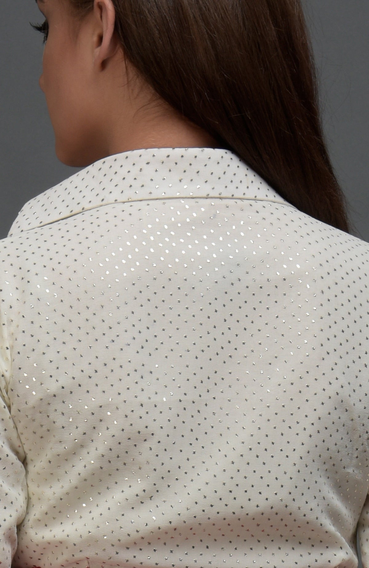 A woman from the back wearing a white blouse with silver polka dots.