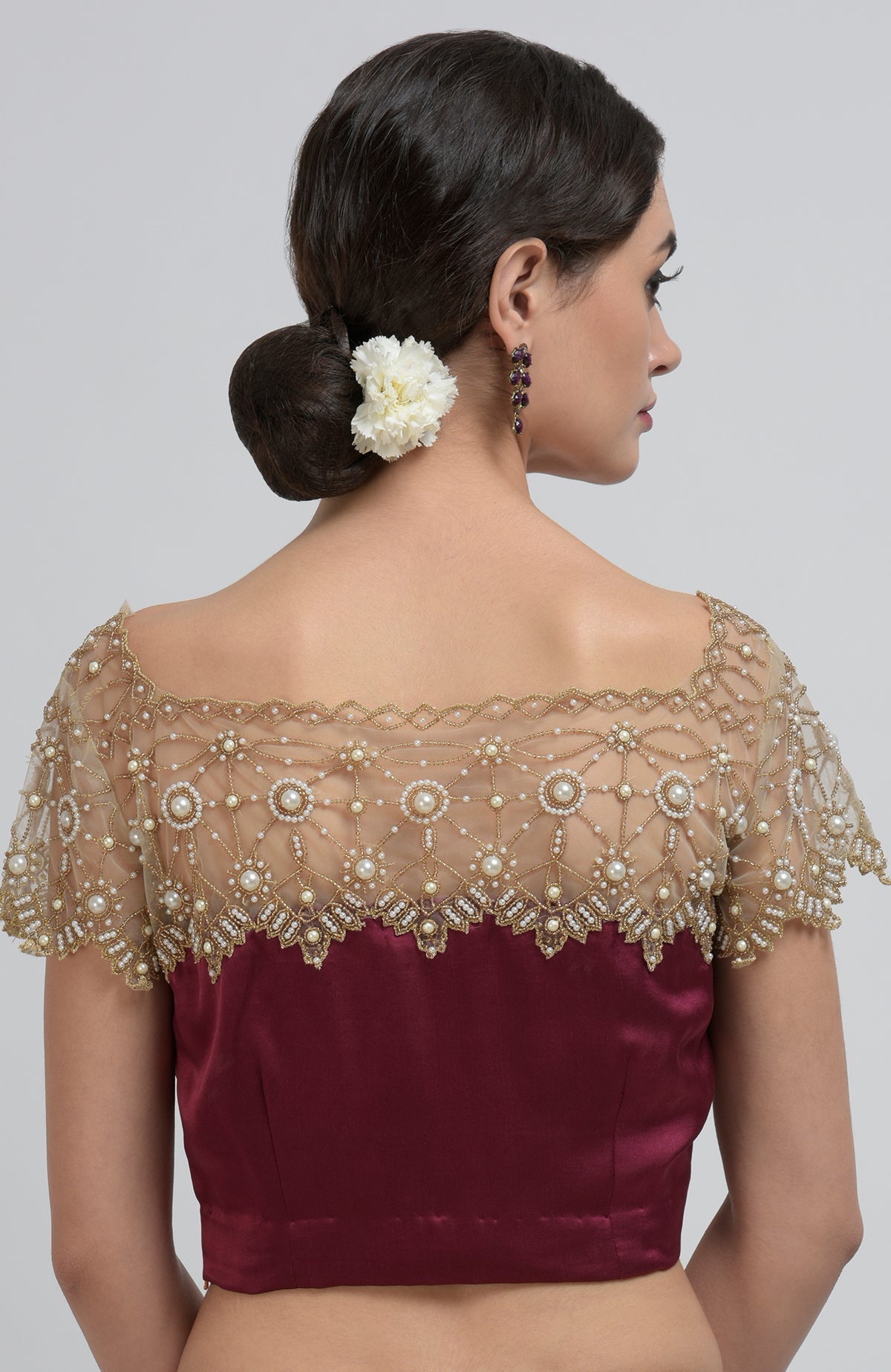 Back view of a woman in a burgundy blouse with a sheer, embroidered back and sleeves.