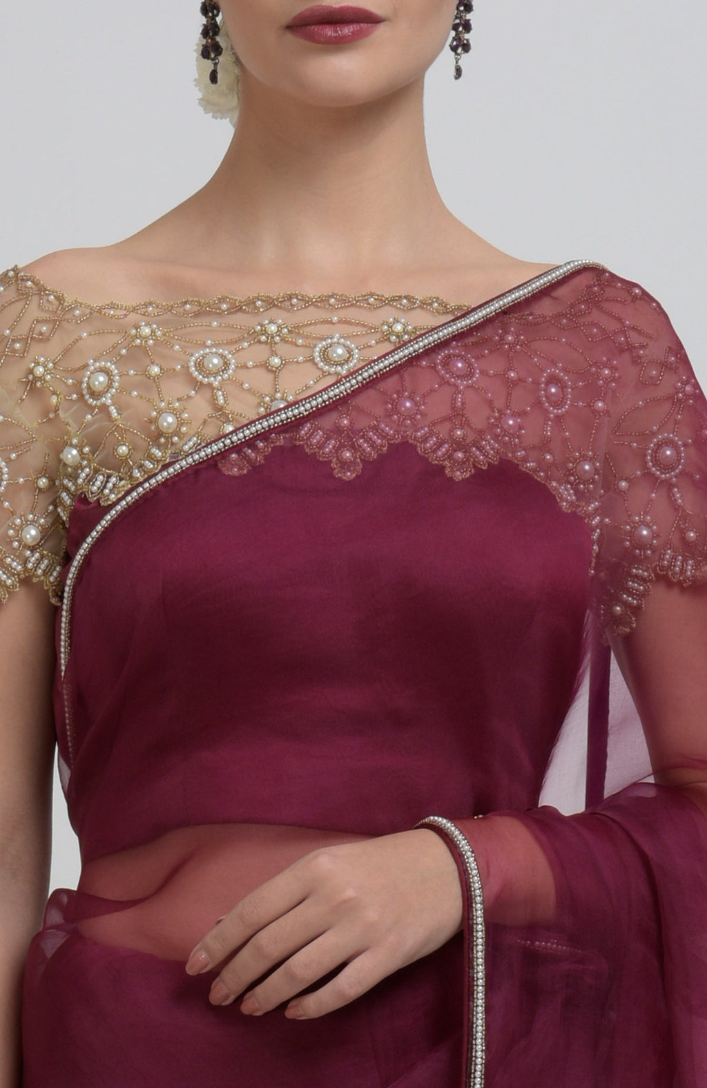 A woman models a burgundy saree with a pearl-beaded blouse and matching border.