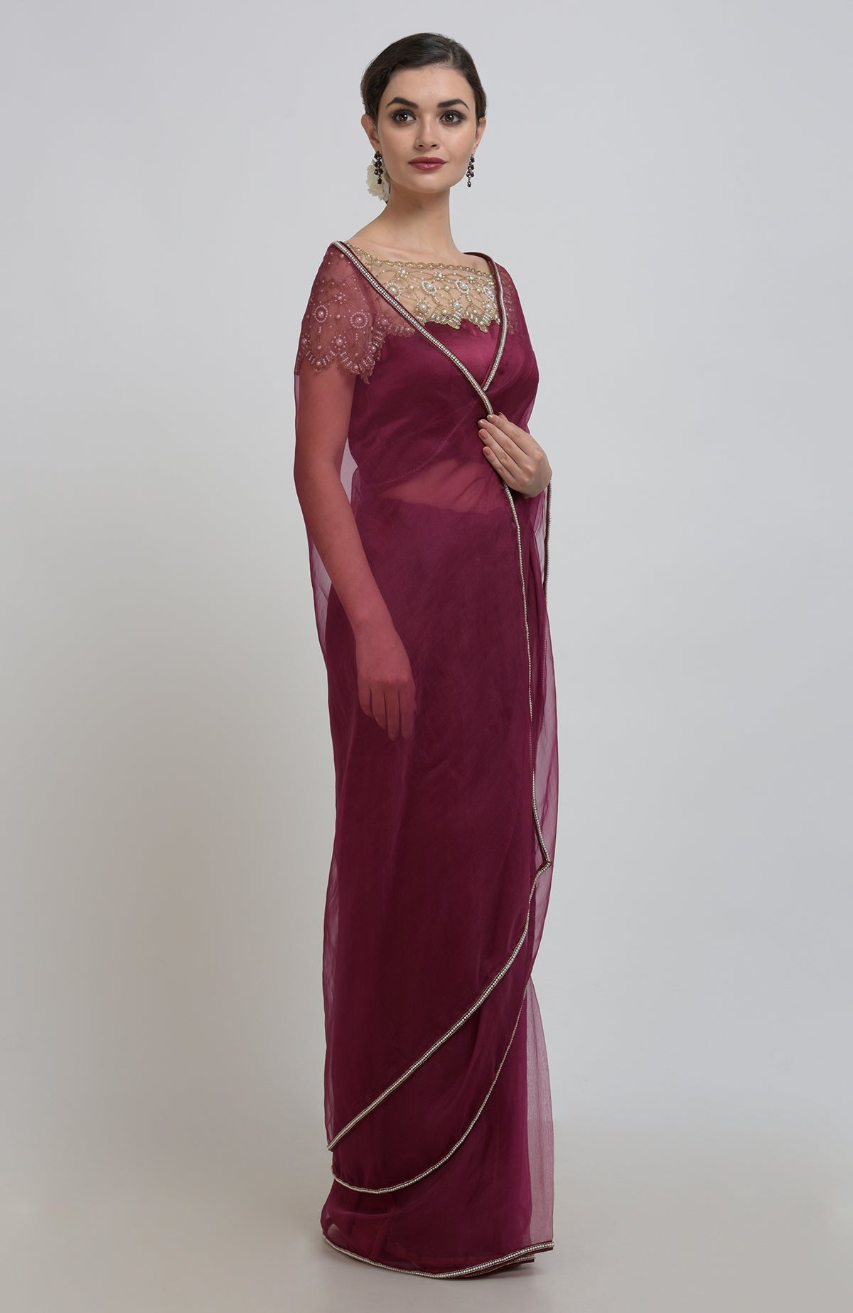 A woman models a burgundy organza saree with pearl bead embroidery and a matching blouse.
