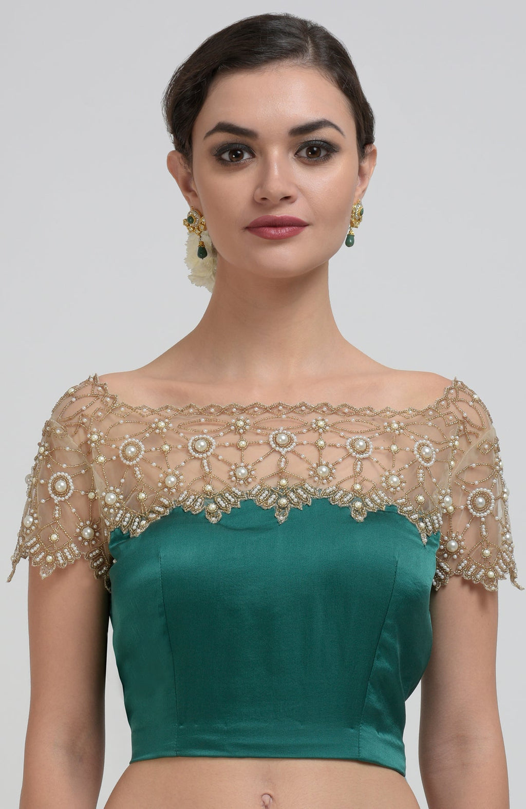 A woman models an emerald green saree and blouse with pearl bead embroidery.