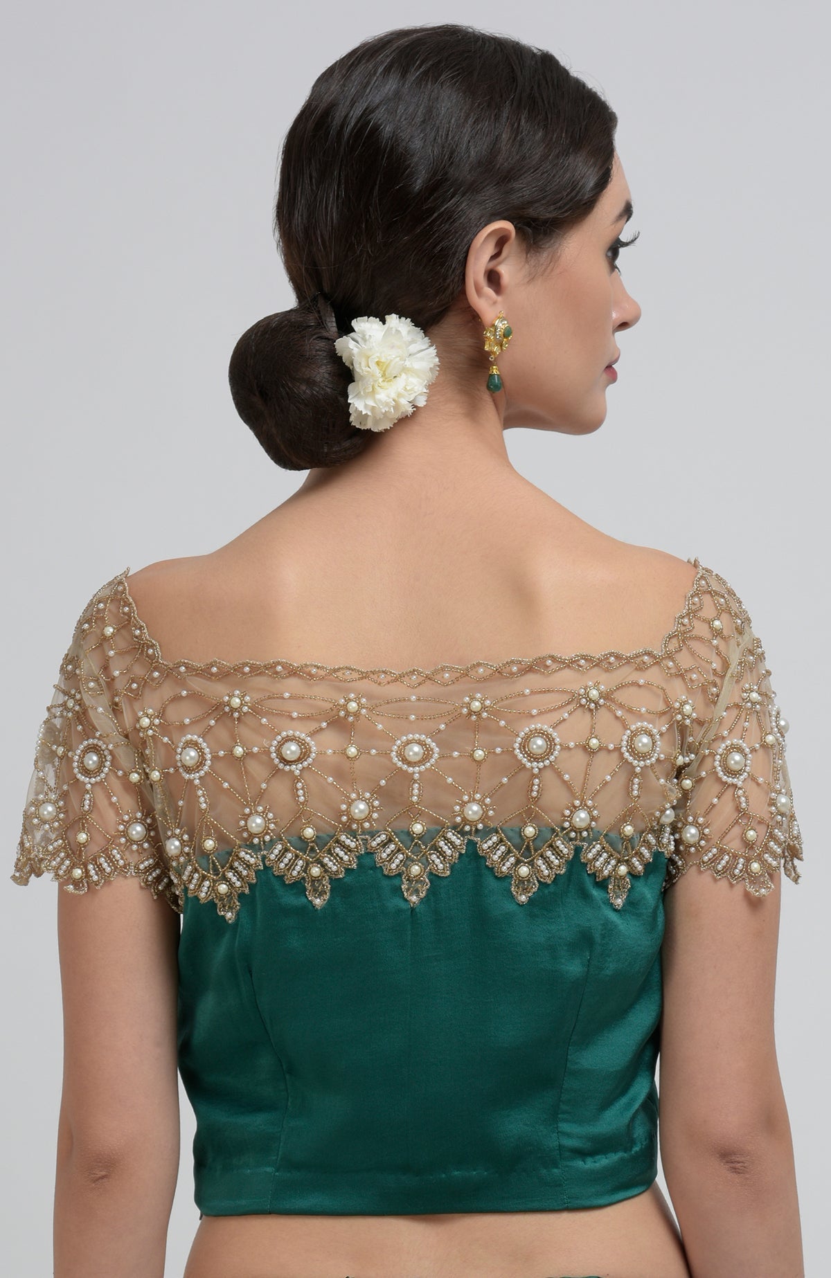 A woman from behind wearing an emerald green blouse with a pearl-beaded sheer neckline.