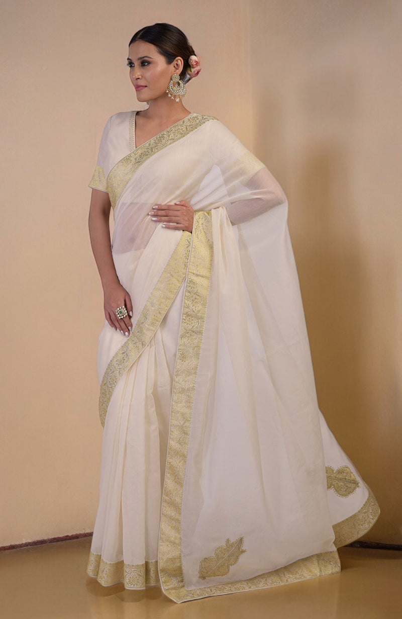 Ivory Banarasi saree with gold woven border and motifs, paired with embroidered blouse with V-neck.