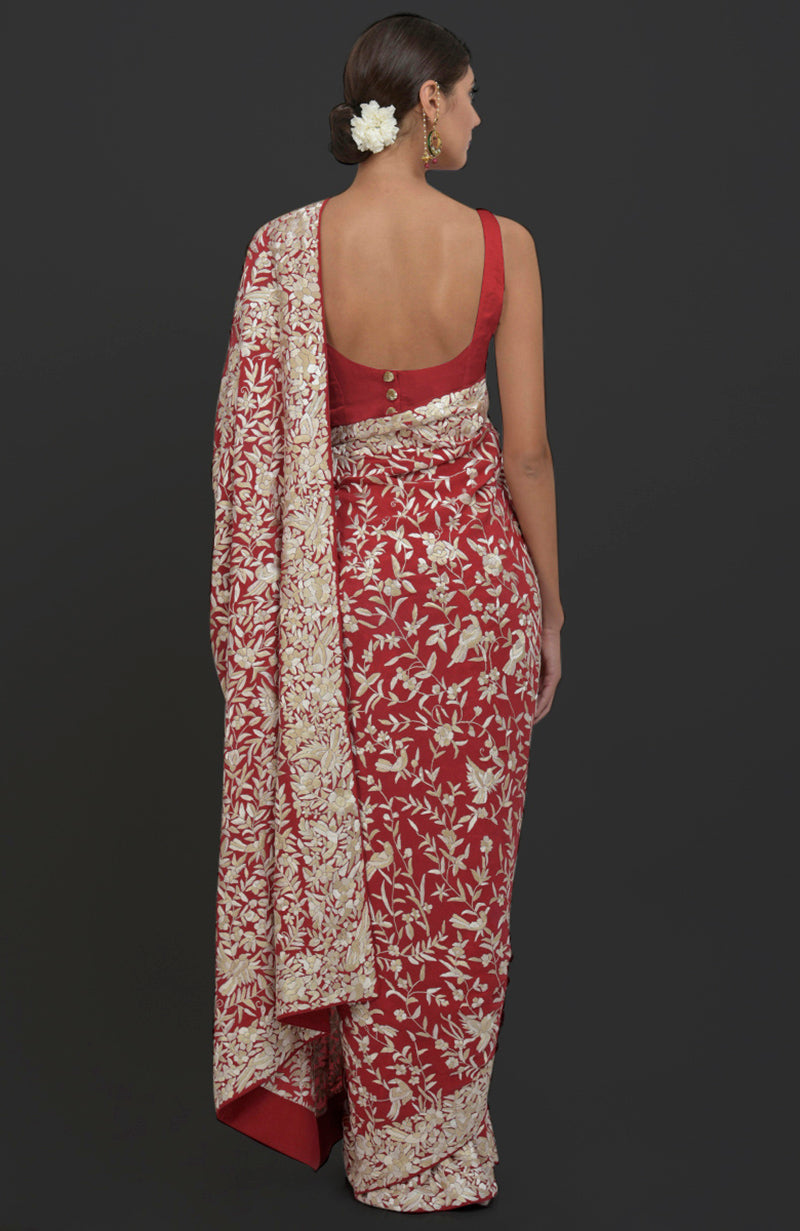 A woman models a red Parsi Gara hand-embroidered saree with a backless blouse.