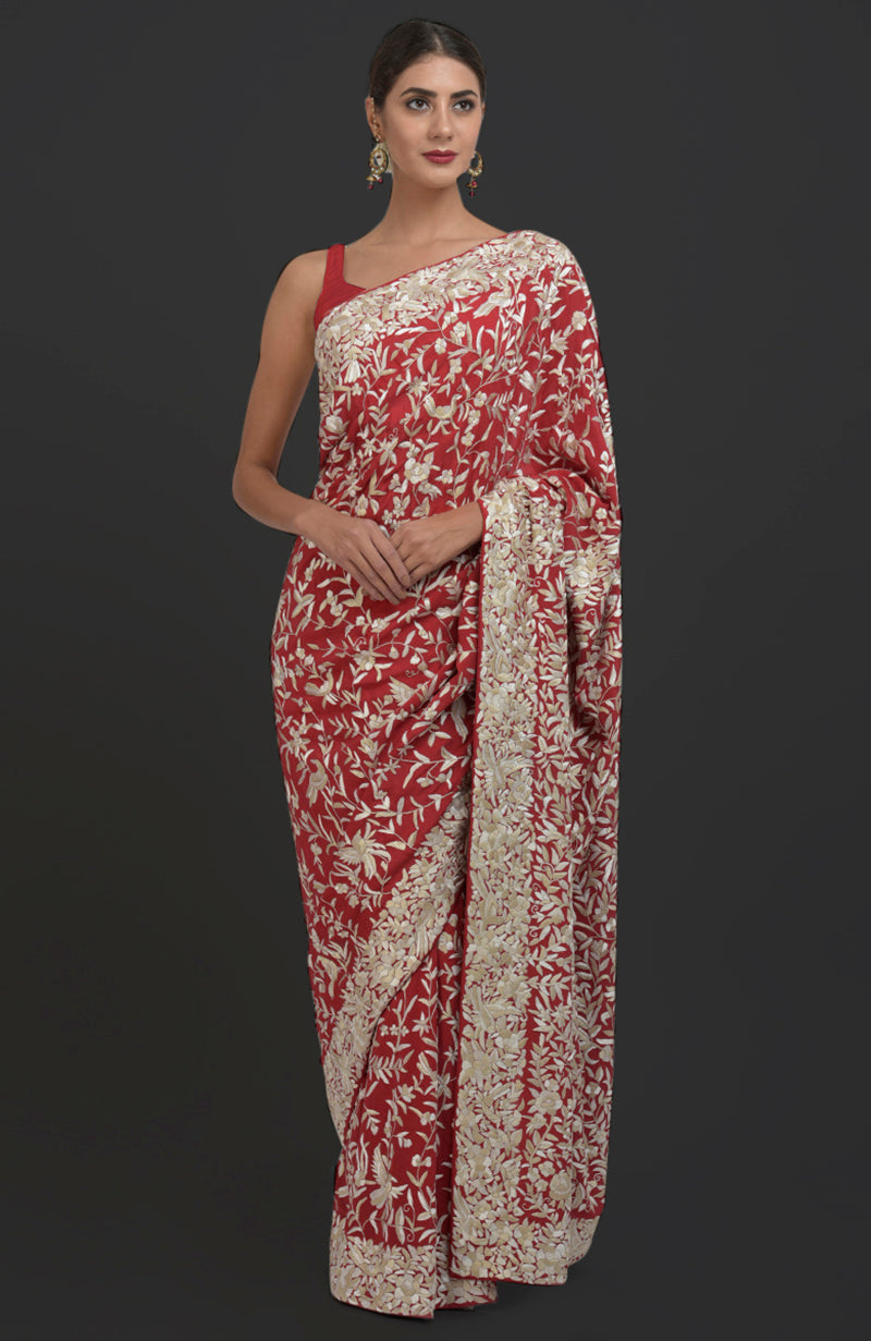 A woman models a red Parsi Gara hand-embroidered saree with floral and bird patterns.