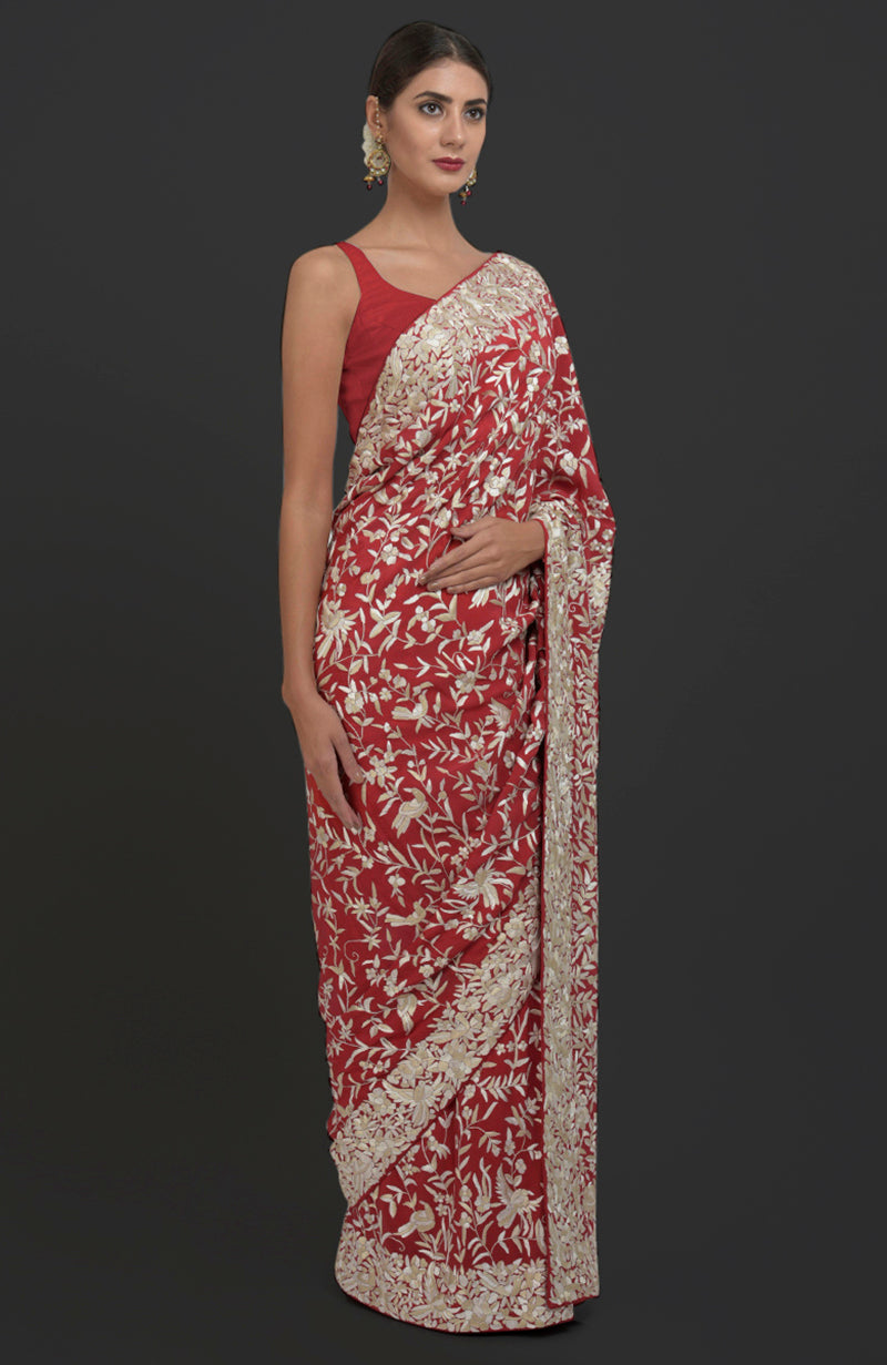 A woman models a red Parsi Gara hand-embroidered saree with floral and bird patterns.