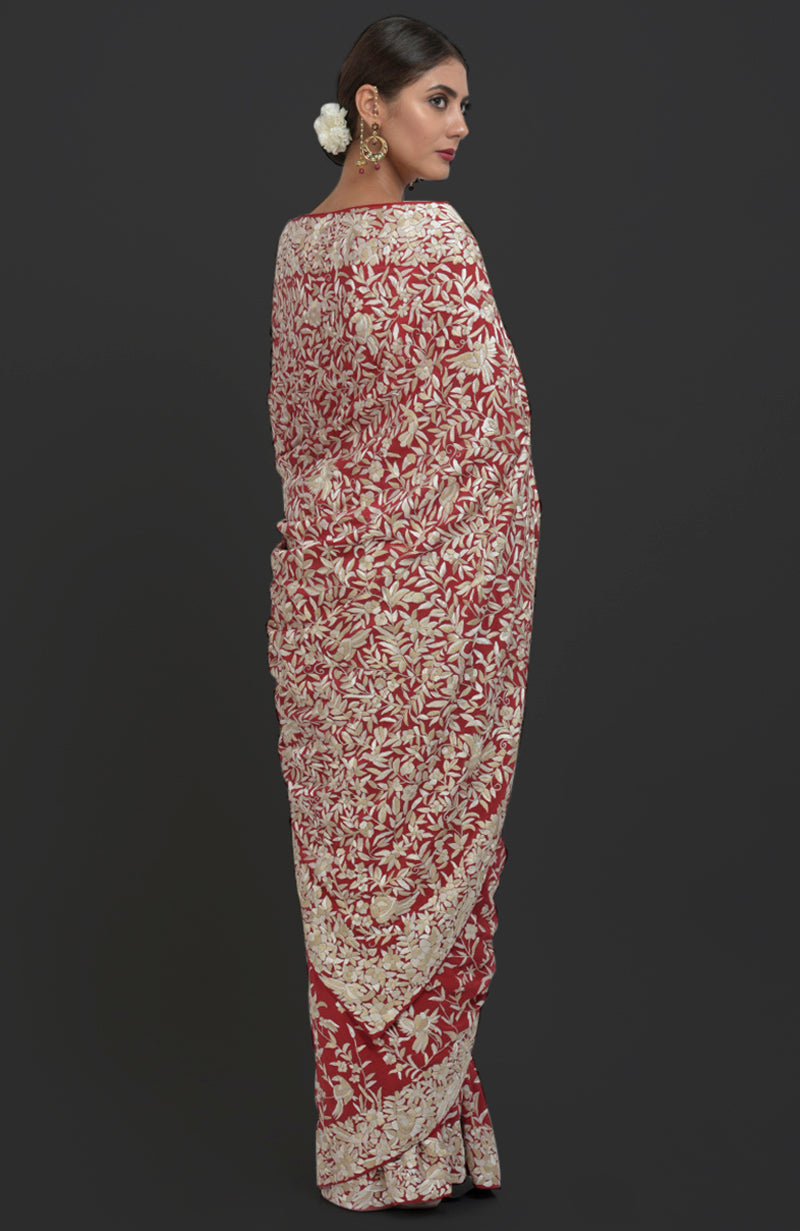 A woman models a red Parsi Gara hand-embroidered saree with floral and bird patterns.