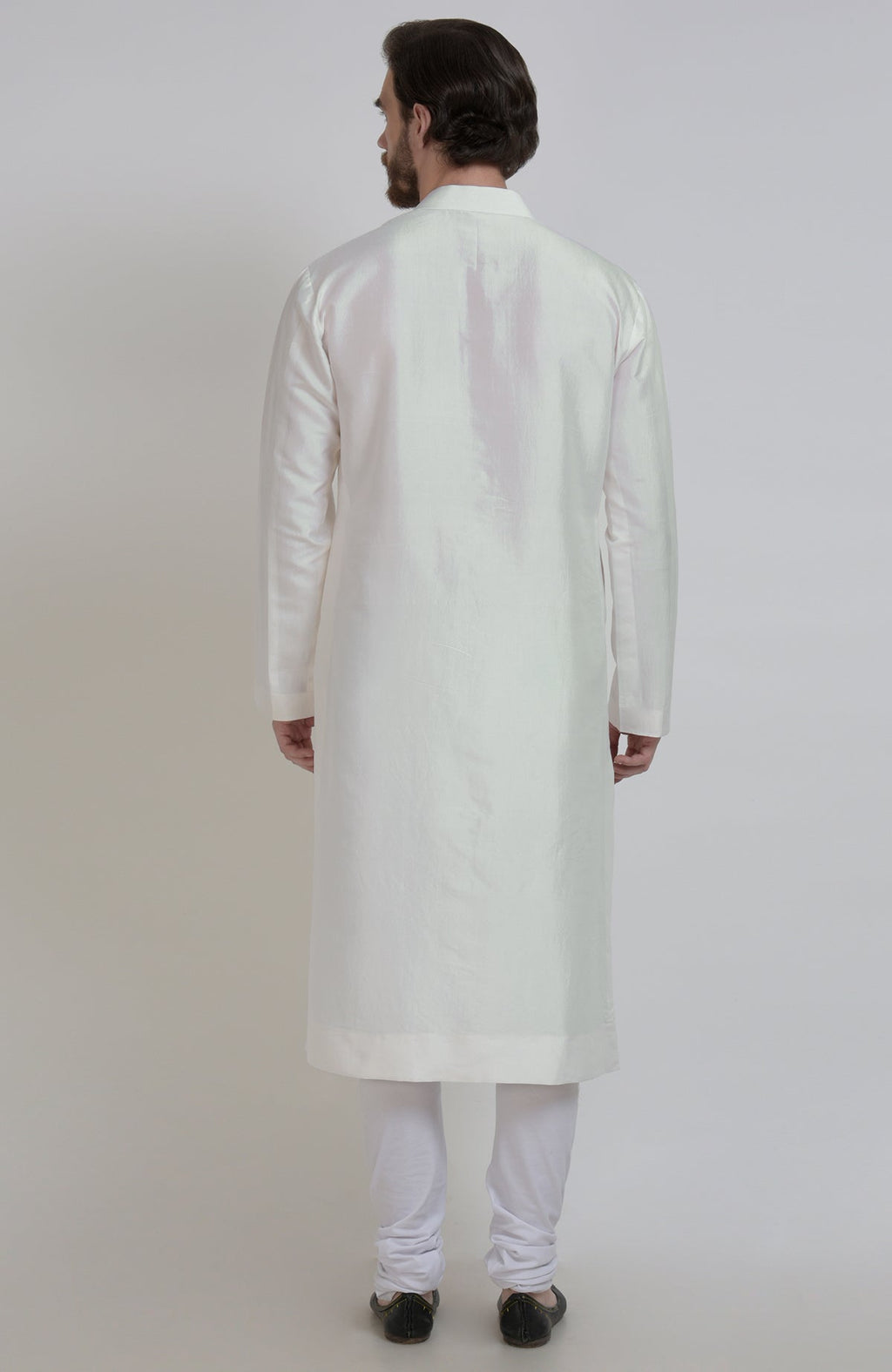 Rear view of a man wearing an ivory silk kurta and white churidar pants.