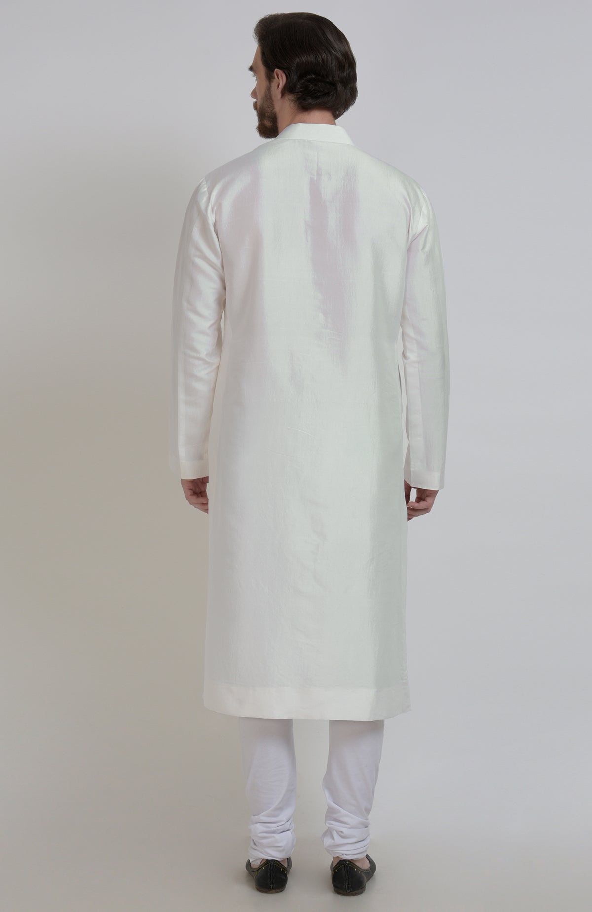 Rear view of a man wearing an ivory silk kurta and white churidar pants.