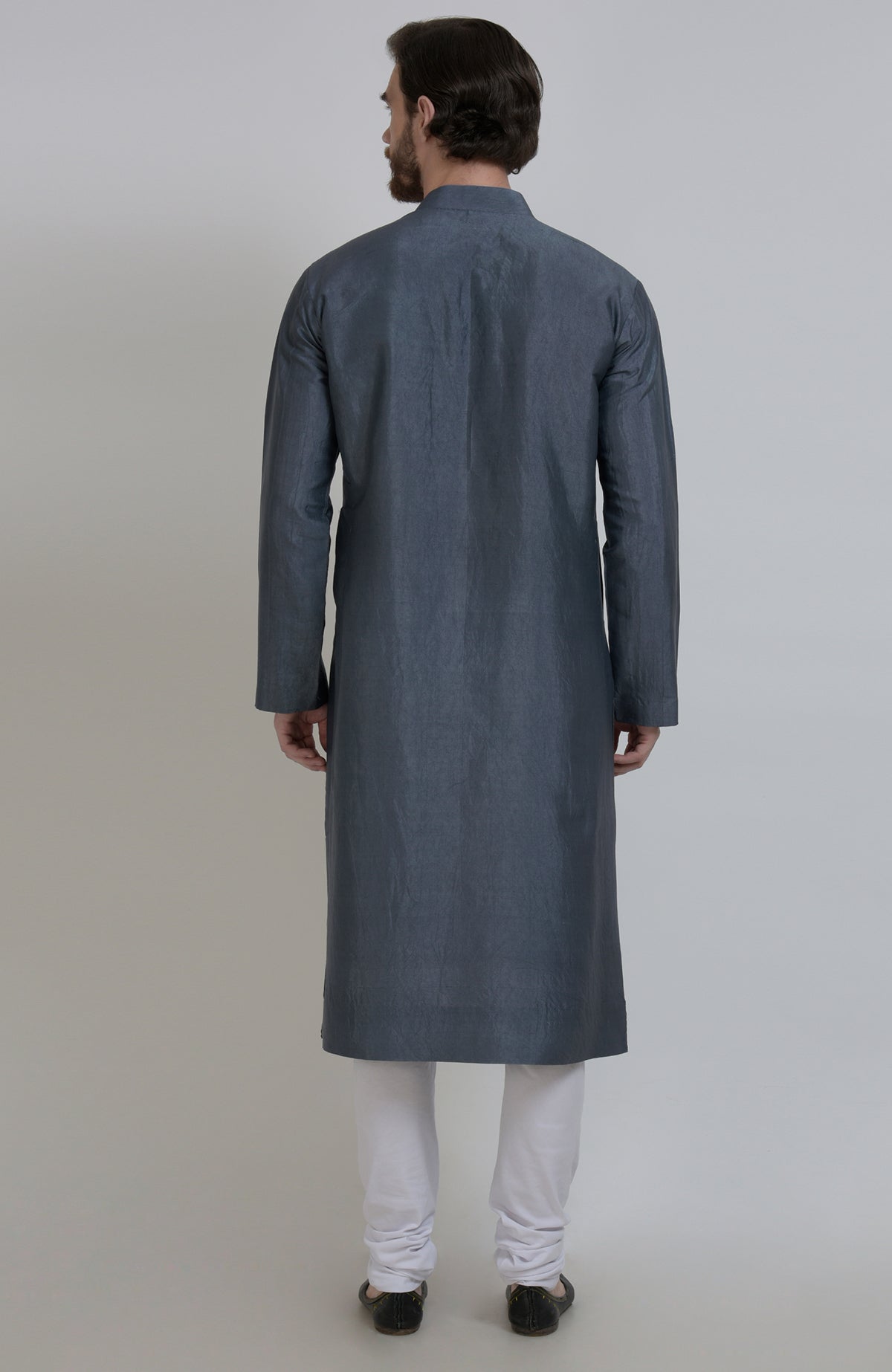 A man from behind wears a grey silk kurta with white churidar pants and black shoes.