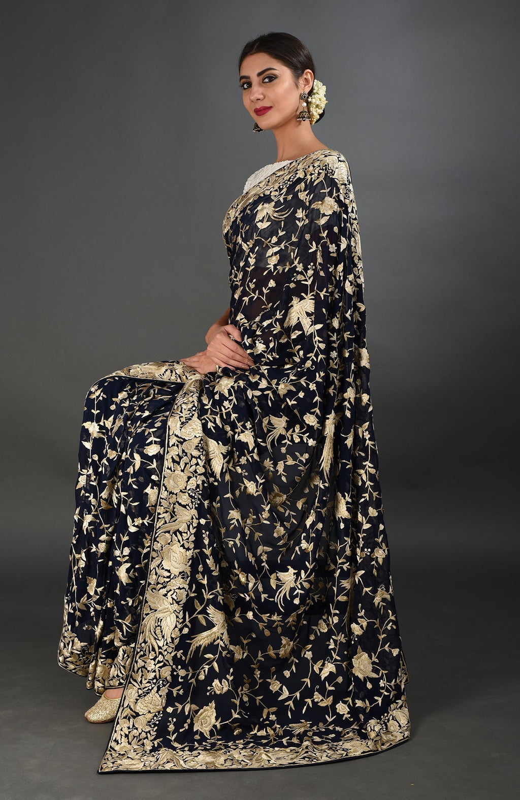 Woman in a midnight blue Parsi Gara hand-embroidered saree with gold floral and bird motifs.