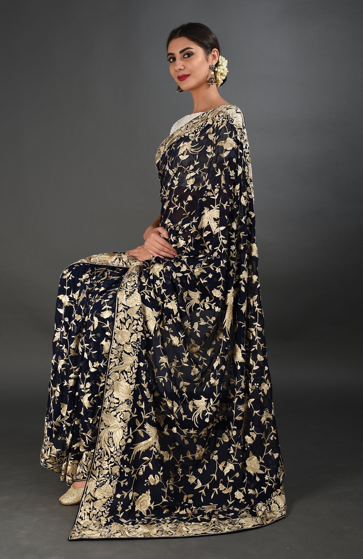 Woman in a midnight blue Parsi Gara hand-embroidered saree with gold floral and bird motifs.