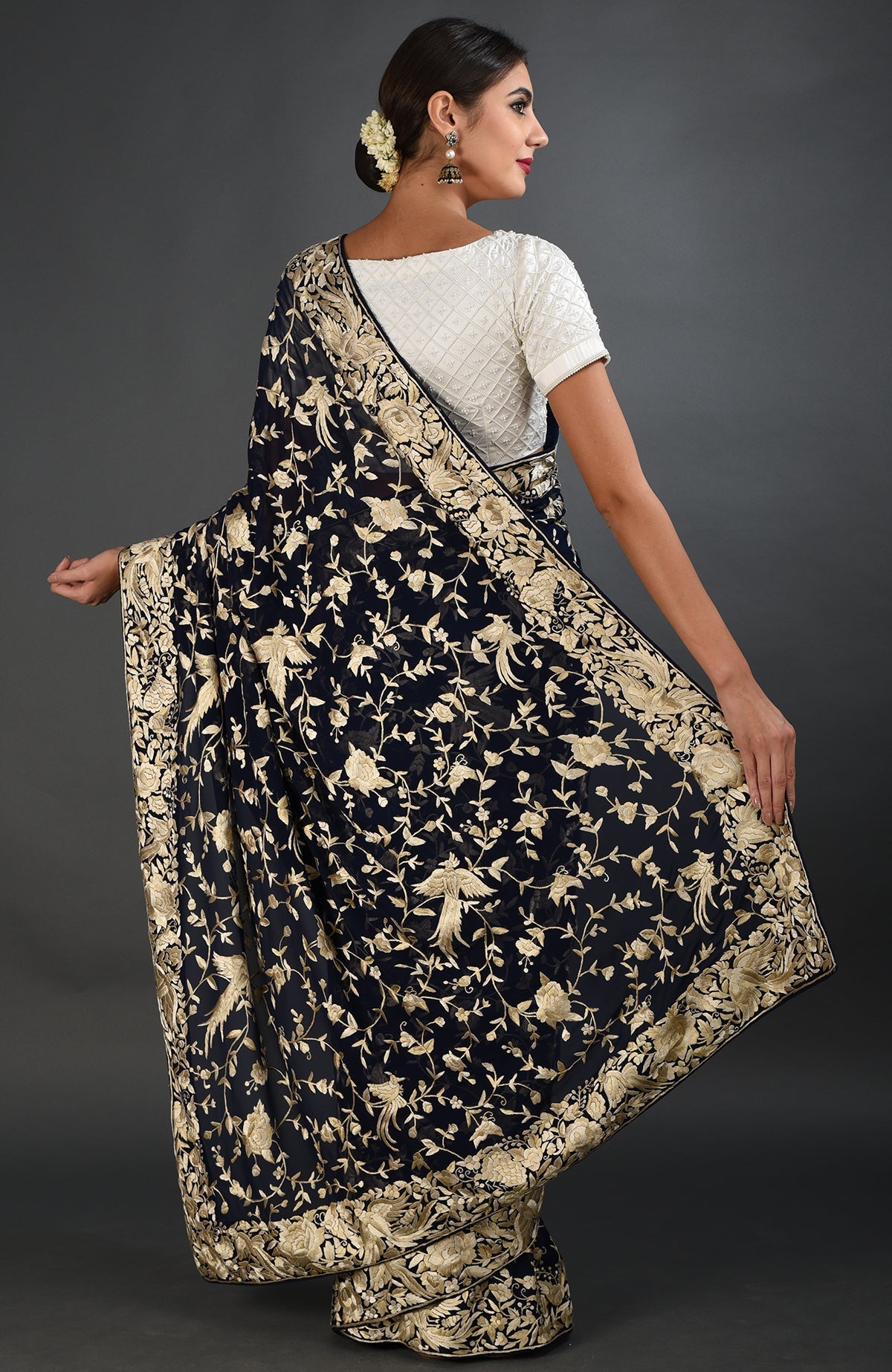 A woman models a midnight blue Parsi Gara hand-embroidered saree with gold birds and florals.