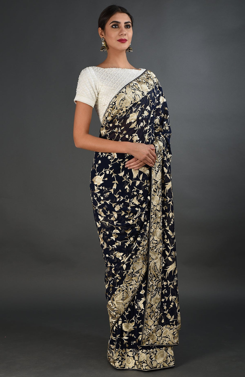 A woman models a midnight blue Parsi Gara hand-embroidered saree with a white blouse.