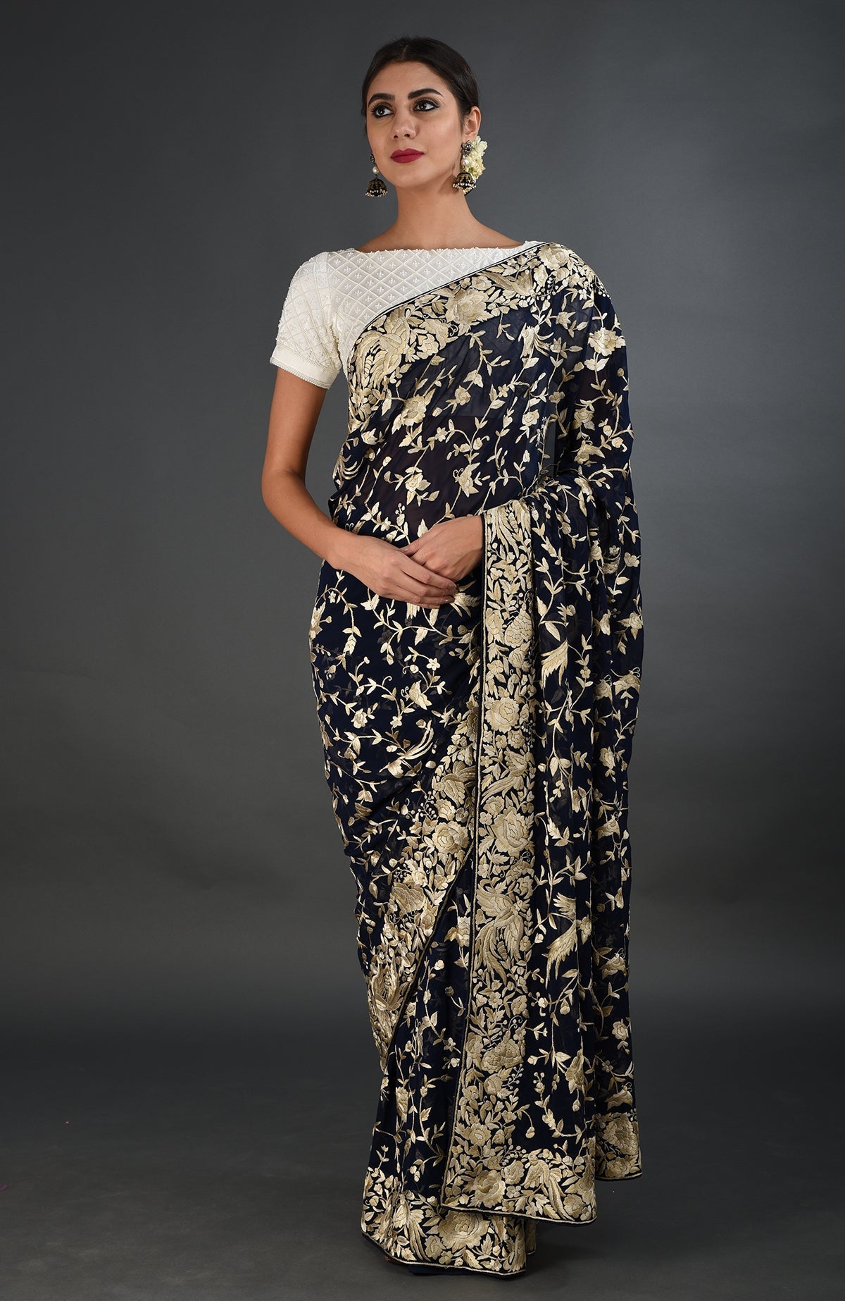 A woman models a midnight blue Parsi Gara hand-embroidered saree with a white blouse.