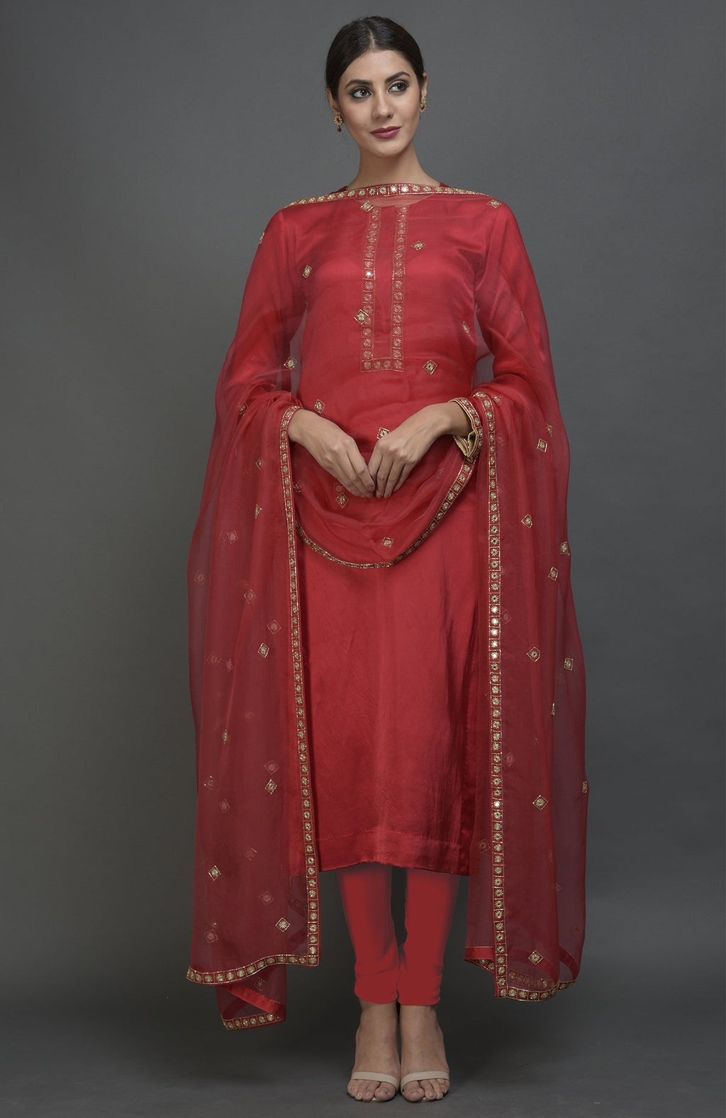 A woman models a red satin silk suit with mirror and zardozi work and a matching dupatta.