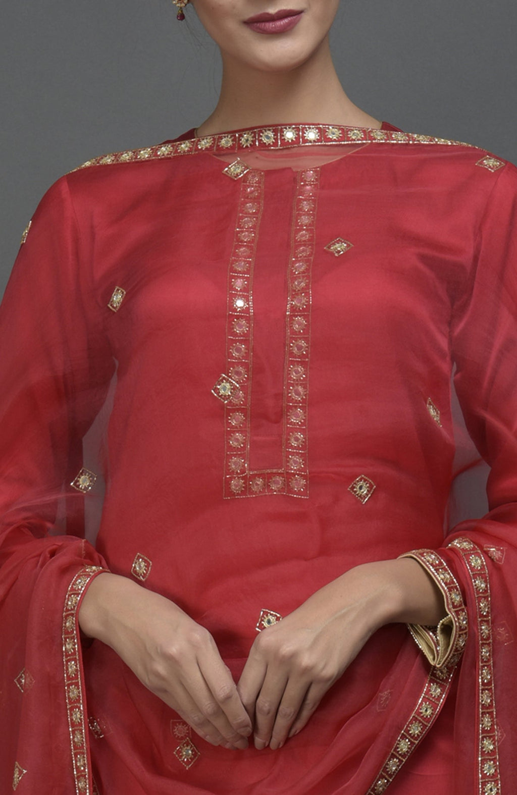A woman models a red mirror and zardozi work suit with a dupatta.