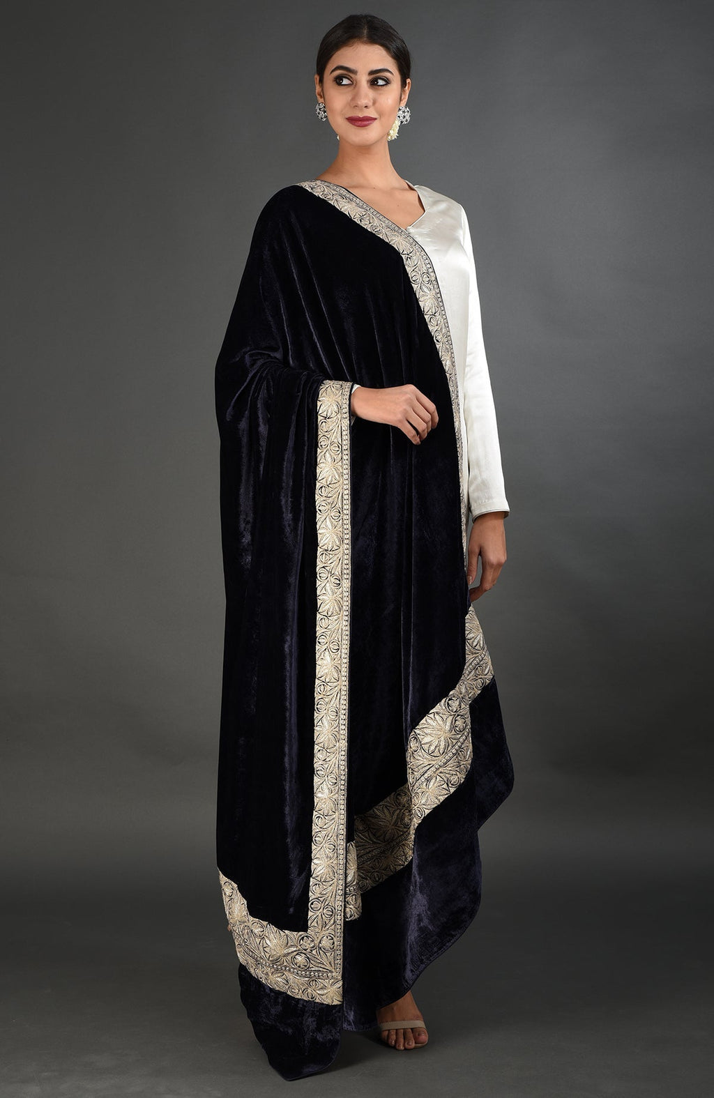 A woman models a midnight blue velvet dupatta with silver tilla embroidery over a white suit.
