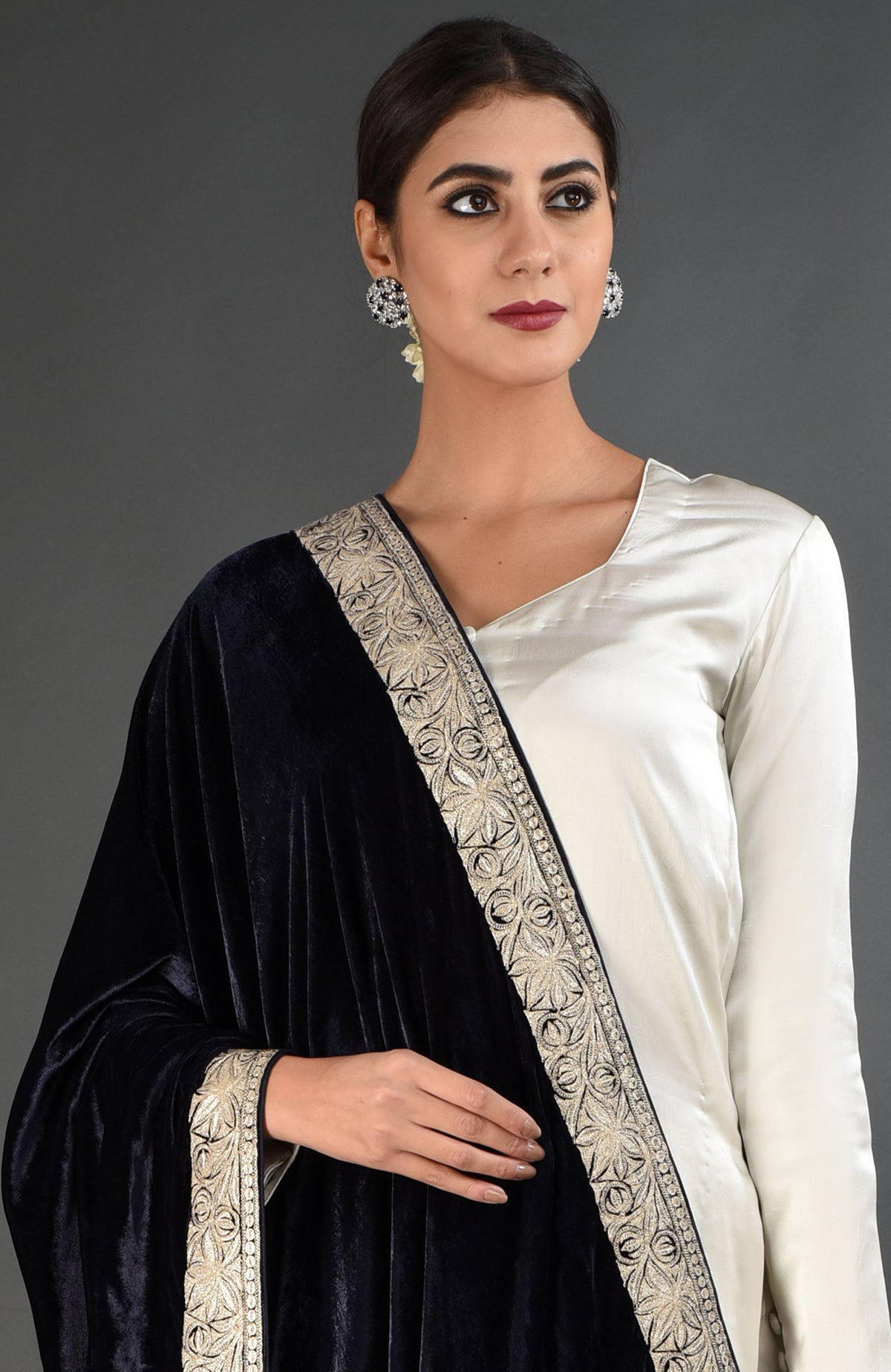 A woman models a midnight blue velvet dupatta with silver tilla embroidery over a white suit.