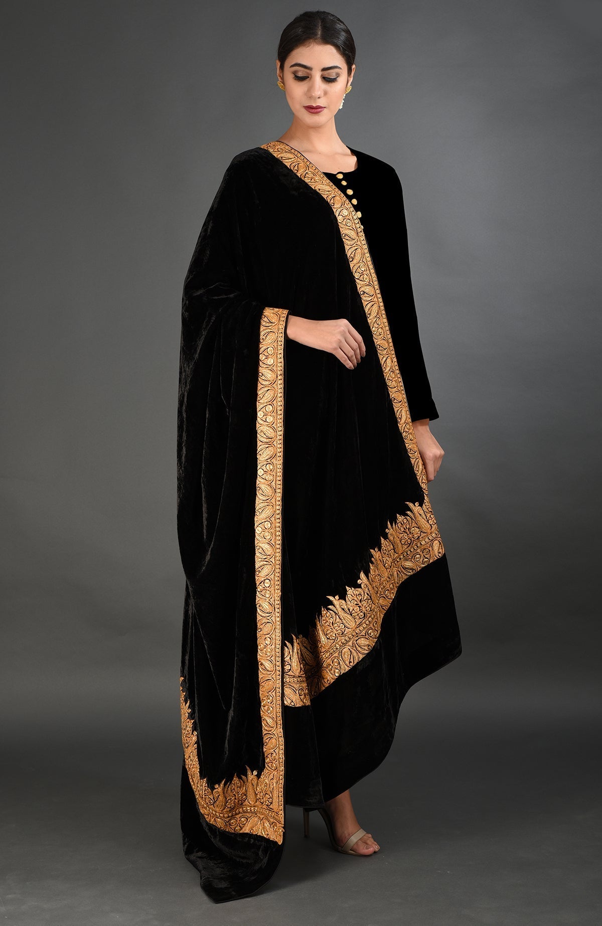 A woman models a black velvet shawl with gold Kashmiri Tilla embroidery.