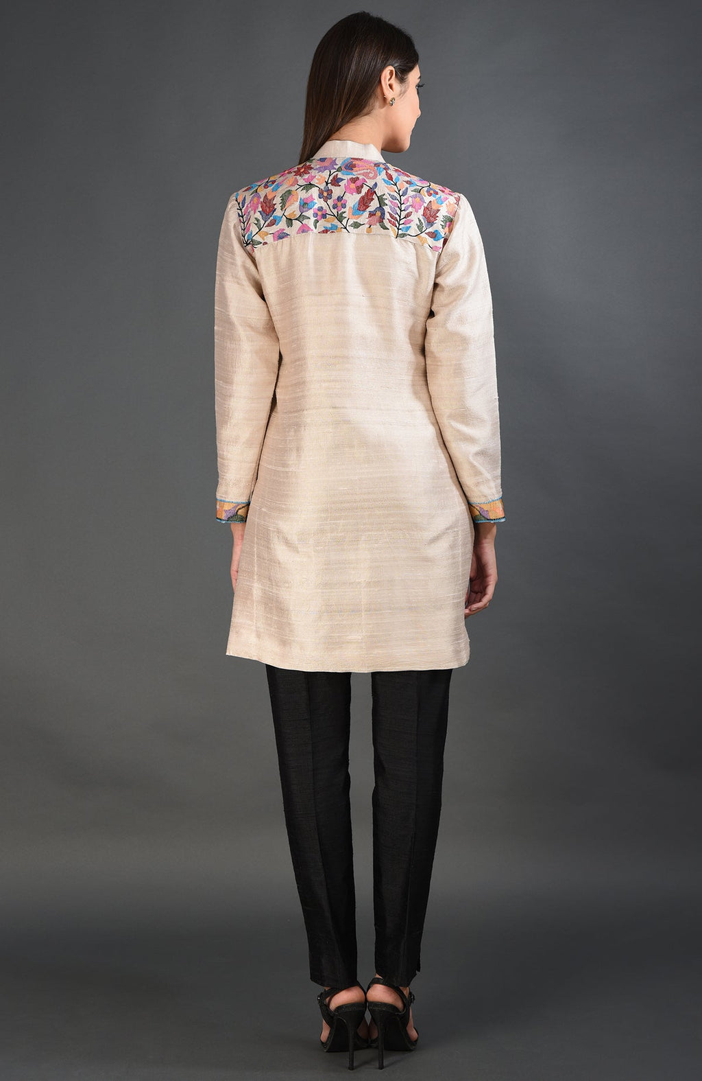 A woman models a creamy beige Kashmir Kani art embroidered jacket with black pants.