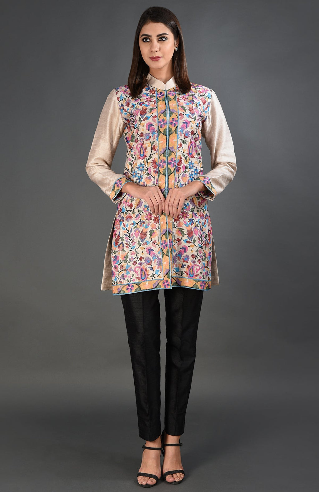 A woman models a creamy beige Kashmir Kani art embroidered jacket with black pants and heels.