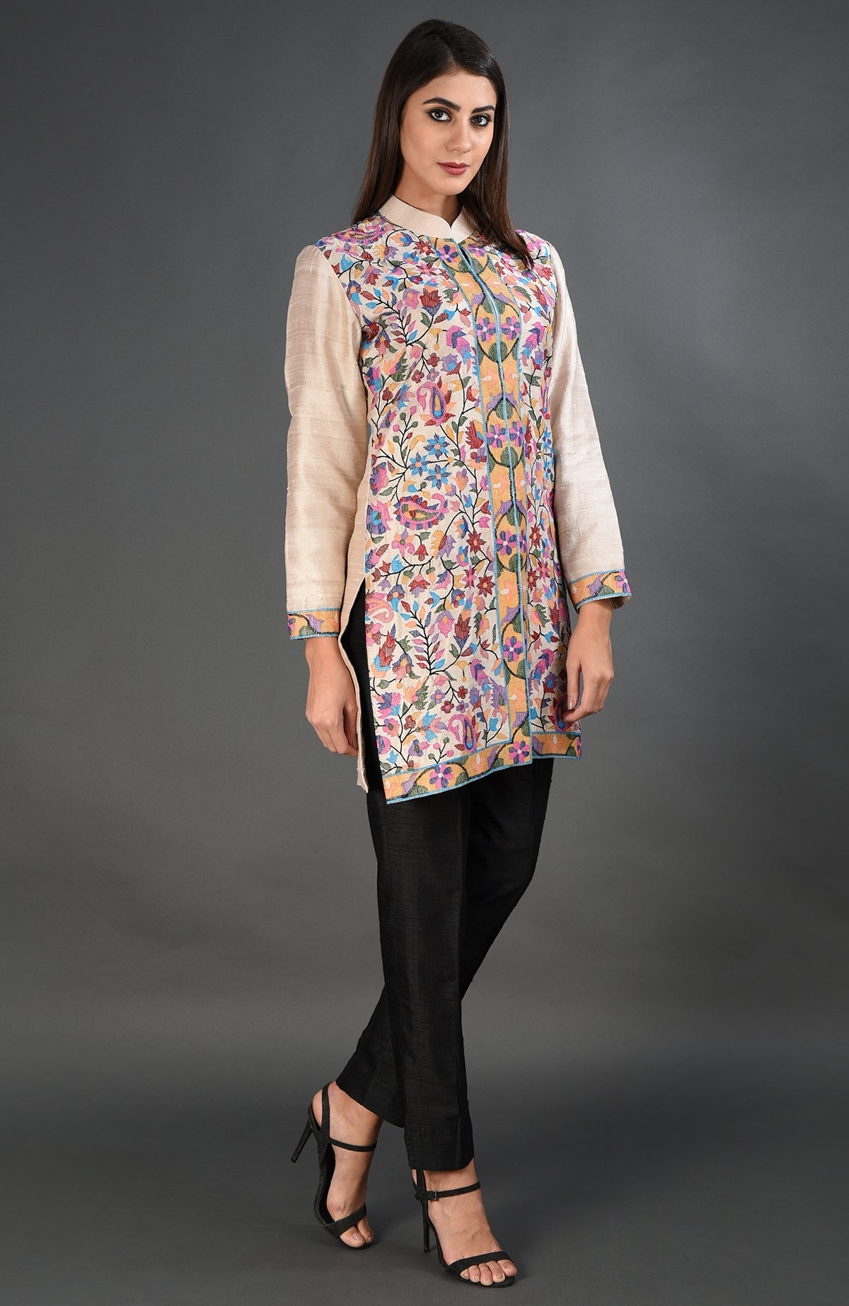 A woman models a creamy beige Kashmir Kani art embroidered jacket set with black pants.