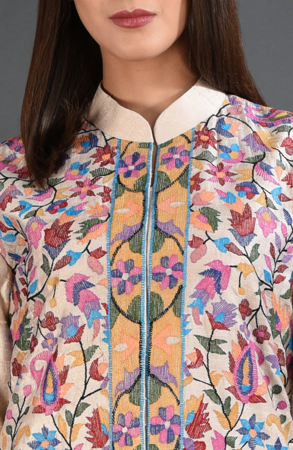 A woman wears a creamy beige jacket with colorful floral and paisley embroidery.