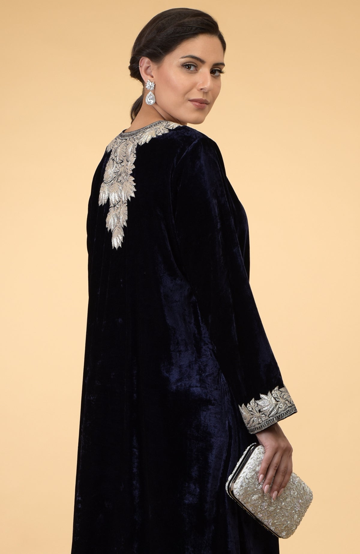 Midnight blue velvet kaftan with silver Kashmir embroidery, worn by a woman holding a clutch.