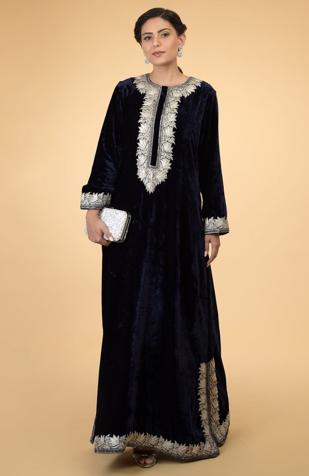 Midnight blue velvet kaftan with silver Kashmir embroidery, held by a woman with a white clutch.