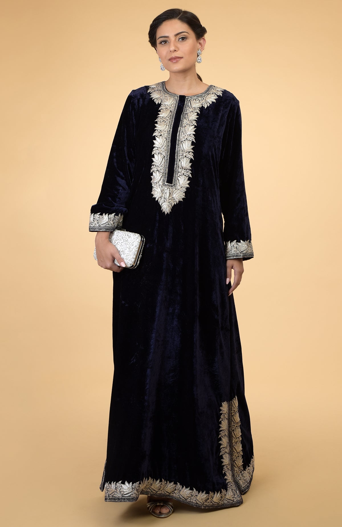 Midnight blue velvet kaftan with silver Kashmir embroidery, held by a woman with a white clutch.