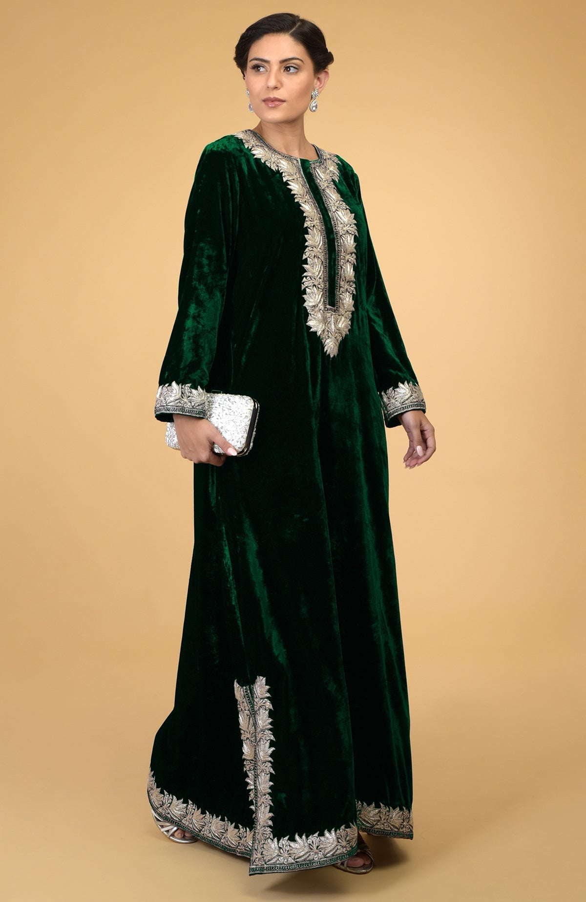 Emerald green velvet kaftan with silver Kashmir embroidery, held by a woman with a white clutch.