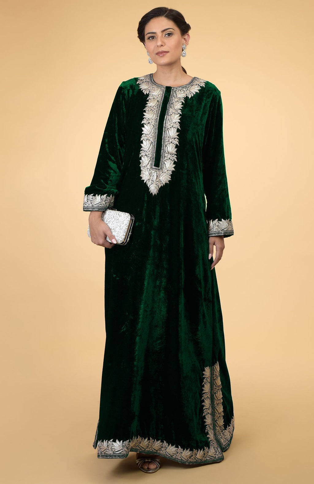 An emerald green velvet kaftan with silver Kashmir embroidery, held by a woman.