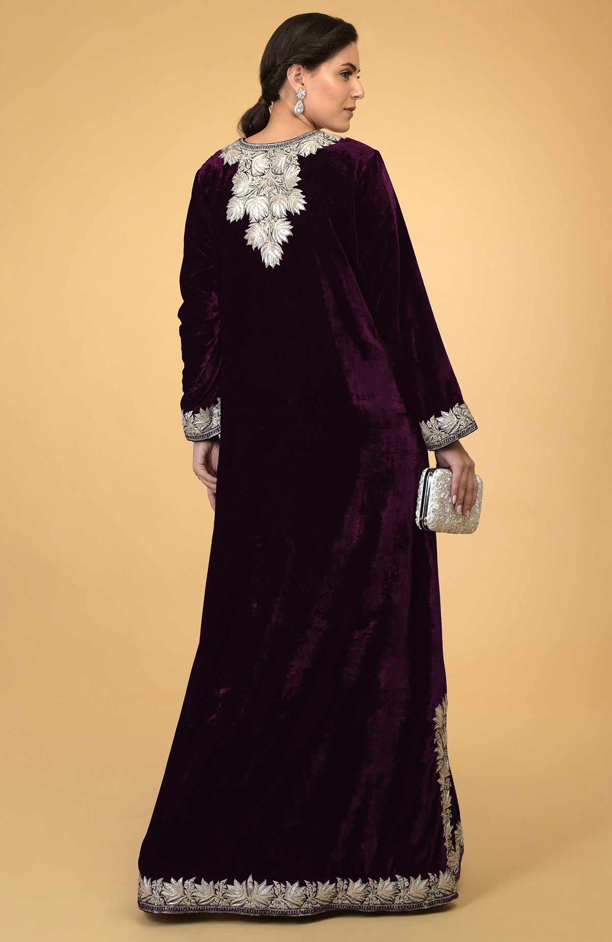 Plum velvet kaftan with silver Kashmir embroidery, held by a woman with a silver clutch.